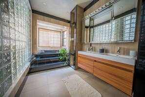 Ein modernes Badezimmer mit einem großen Spiegel, einem Holztischchen und einer Wand aus Glasbausteinen.
