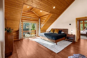 A bedroom with a sloped ceiling, a bed, a nightstand, a lamp, and a view through a glass door.