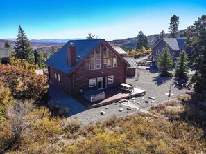 A log cabin with a large deck, surrounded by trees and a clear sky.