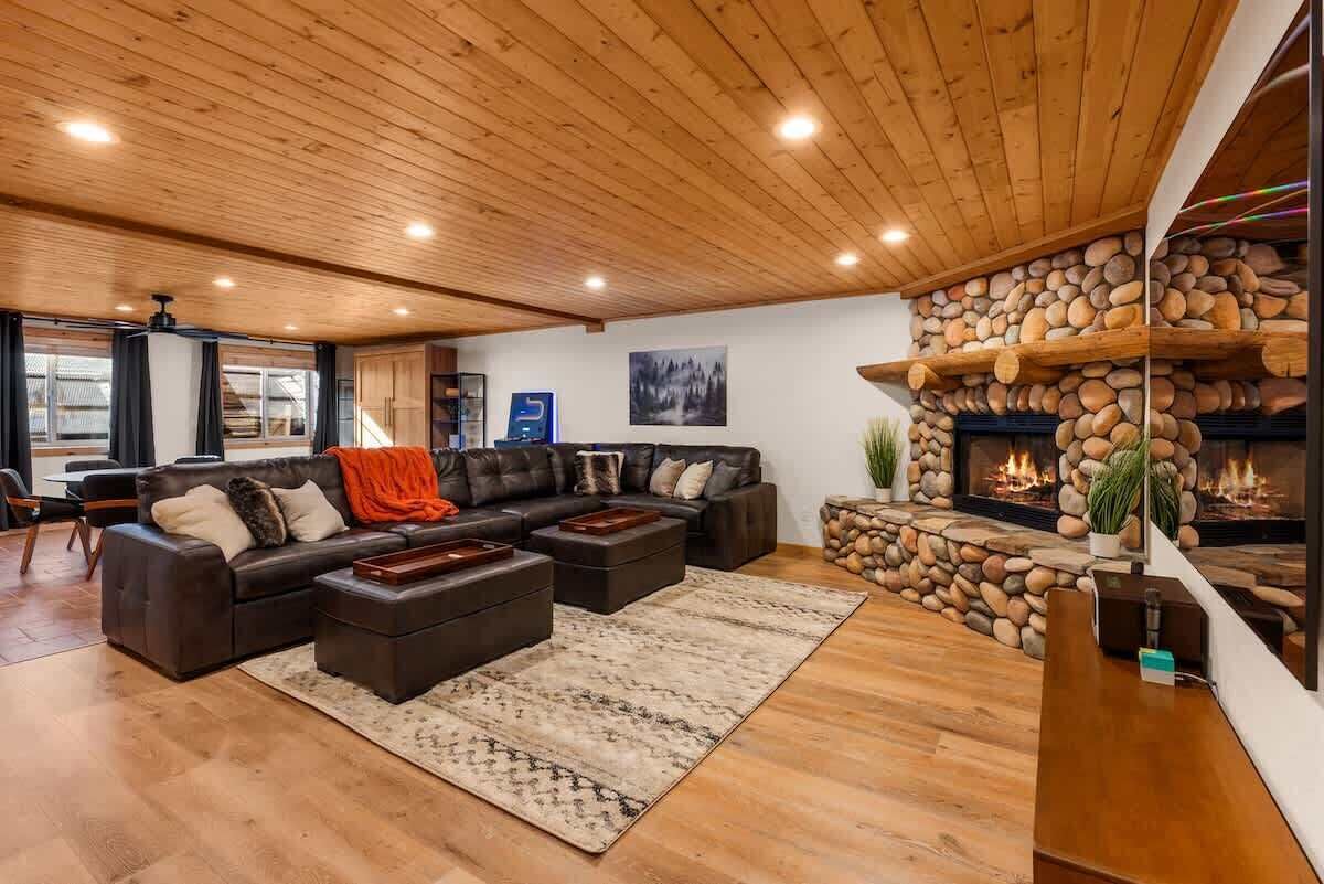 A spacious living room with a stone fireplace, leather sofas, and a wooden ceiling.