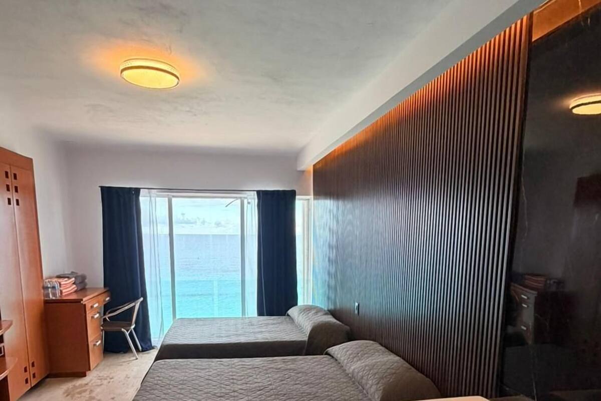A modern hotel room with a large bed, a separate sofa bed, a jacuzzi, a desk with a chair, and a view of the sea.