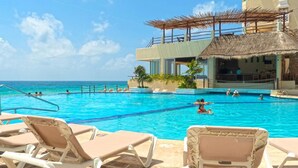 A pool area with lounge chairs, a thatched-roof structure, and a view of the ocean. - Suites Luna y Sol Caribe (Cancún)