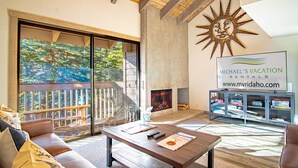 Un'ampia zona giorno con soffitto in legno, una grande finestra con vista su una terrazza, un camino e un cartello di Michael's Vacation Rentals.