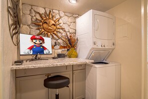 Eine Küche mit Steinwand, einer Waschmaschine, einem Mario-Monitor und einem Barhocker.