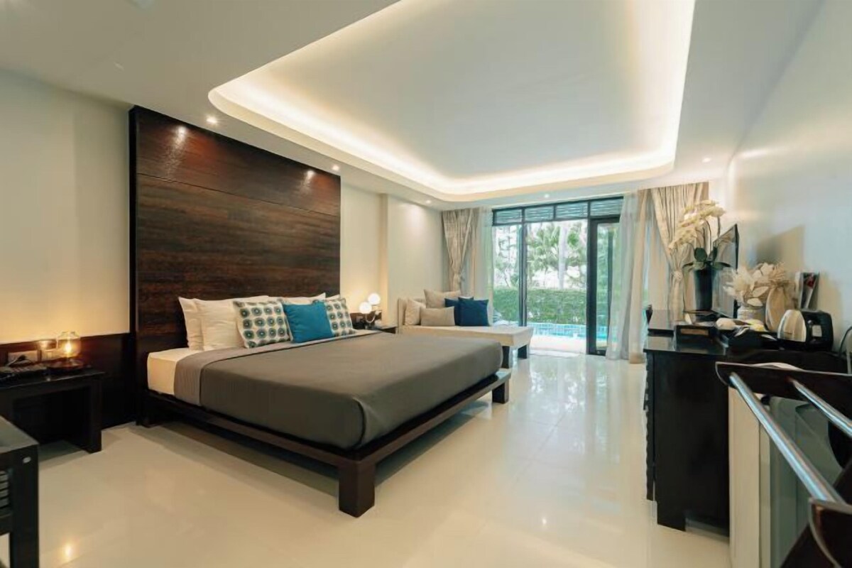 A modern bedroom with a large bed, a nightstand, a desk, and a view of the outdoors.