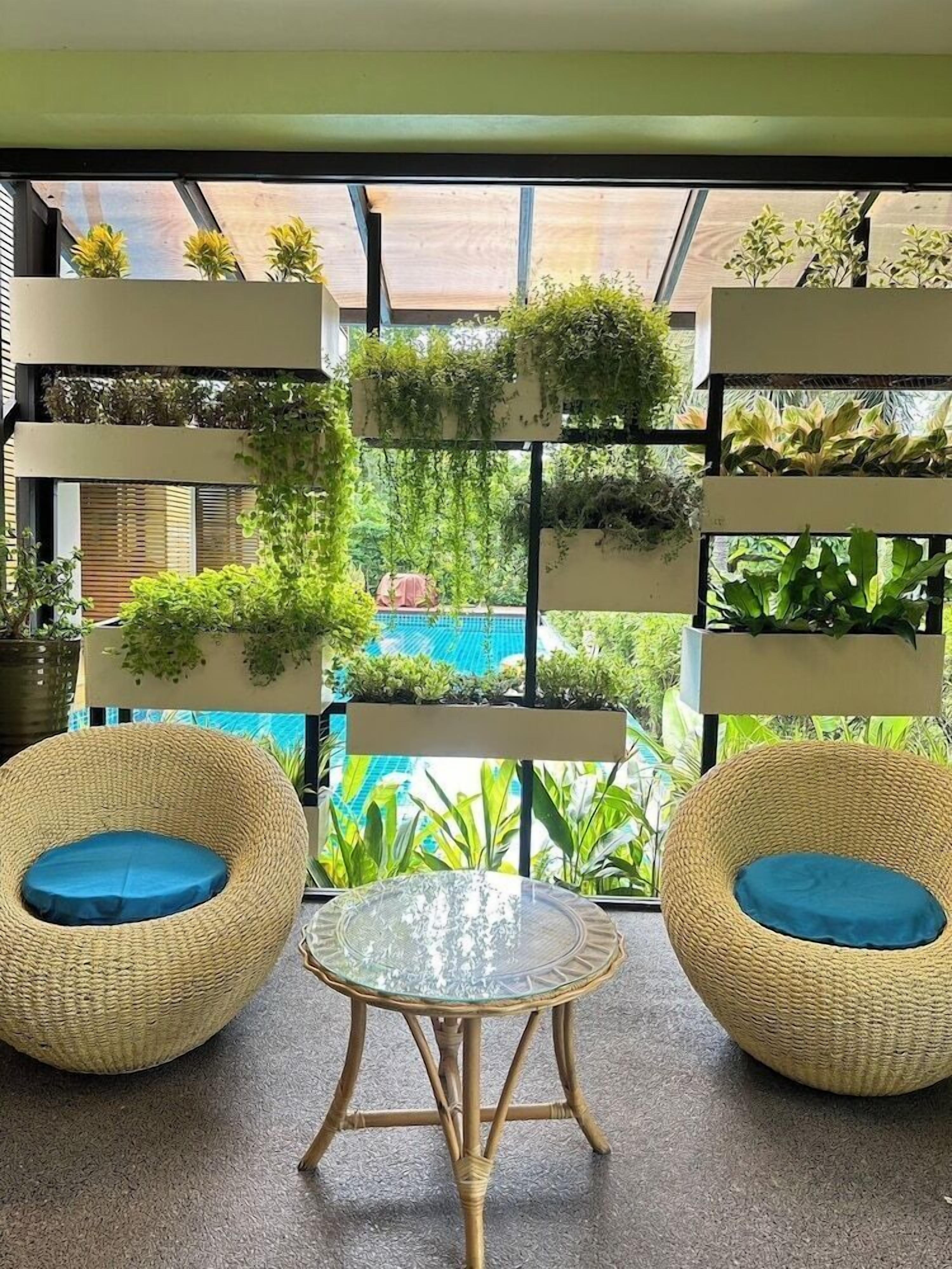 Una habitación con dos sillones de mimbre, una mesa de vidrio y un jardín vertical con plantas.