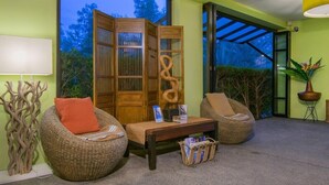 Un espace salon accueillant, avec des fauteuils en osier, une cloison en bois et une petite table sur laquelle sont posés des magazines.