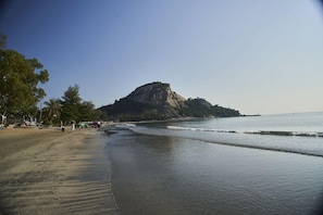 Ein Strand mit einem markanten Felsen, blauem Himmel und ruhigem Wasser.