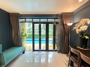 Ein Zimmer mit einer Couch, einem Esstisch, einer Lampe und Blick auf einen Pool durch eine Glasdoor.