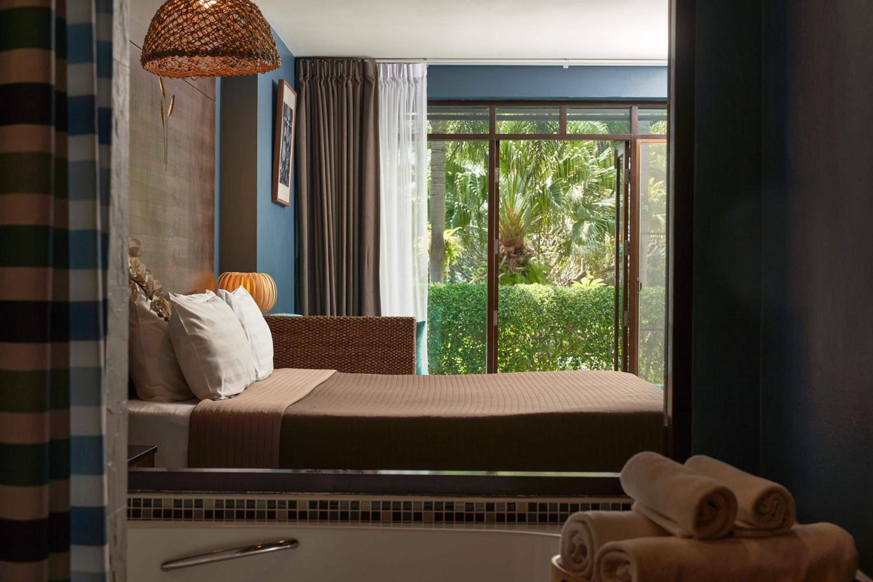 A bedroom with a large window, a bed, a bedside table, and a hanging light fixture.
