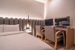 A hotel room with a bed, a desk with a computer, and a chair.