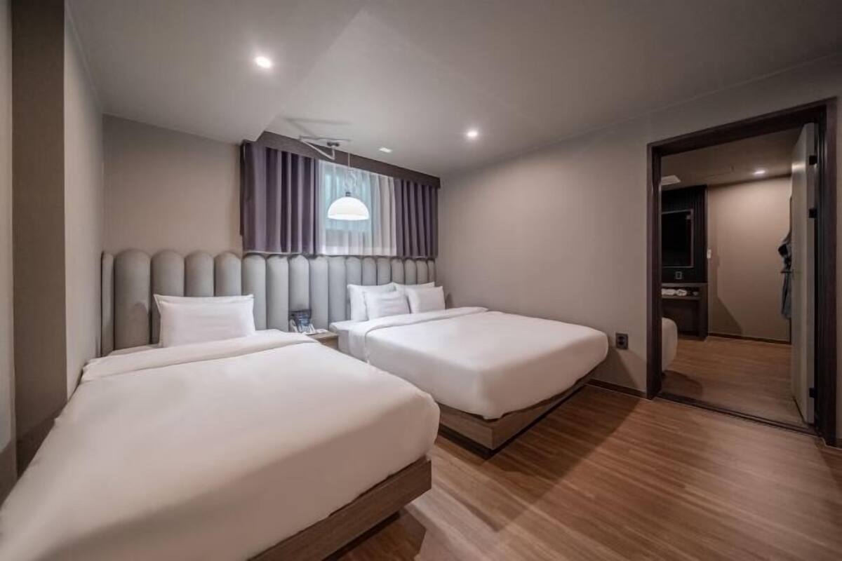 A hotel room with two beds, a large mirror, and a wooden floor.