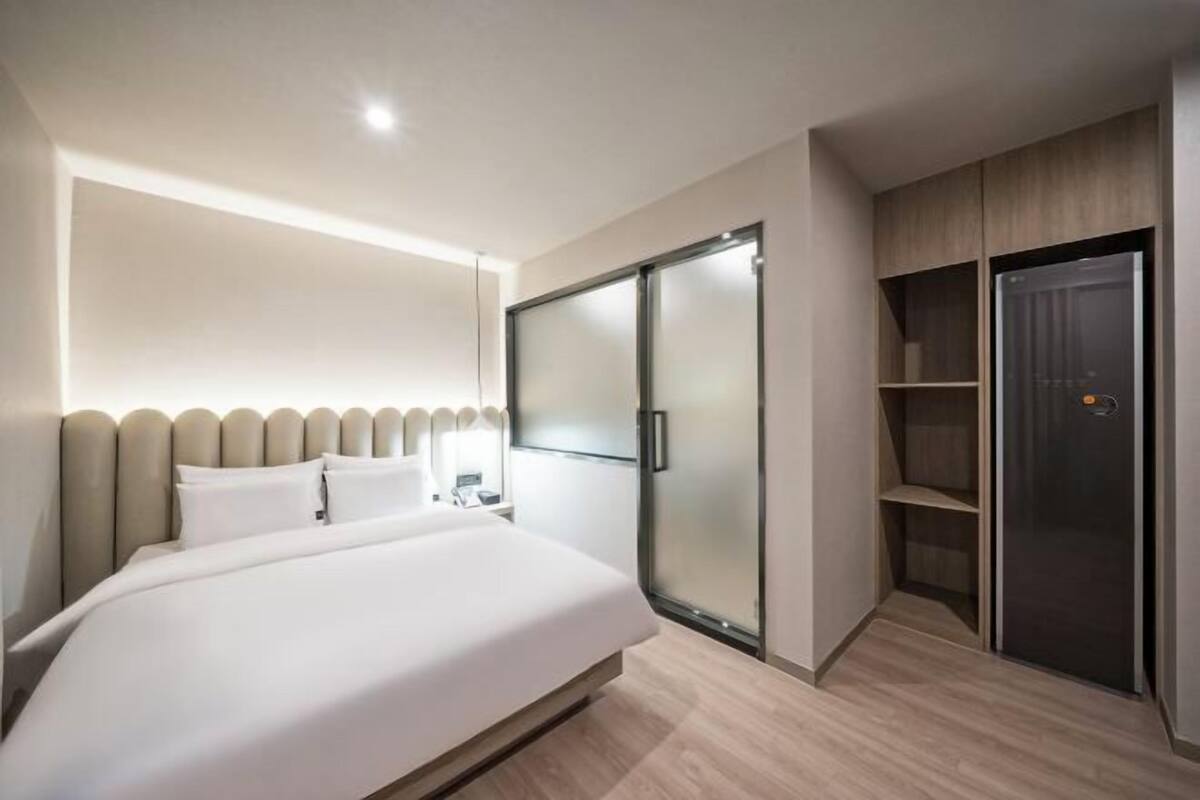 A modern hotel room with a large bed, a sliding glass door closet, and a built-in wardrobe.