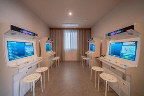 A room with four gaming stations, each with a screen and control panel, and a central window with curtains.
