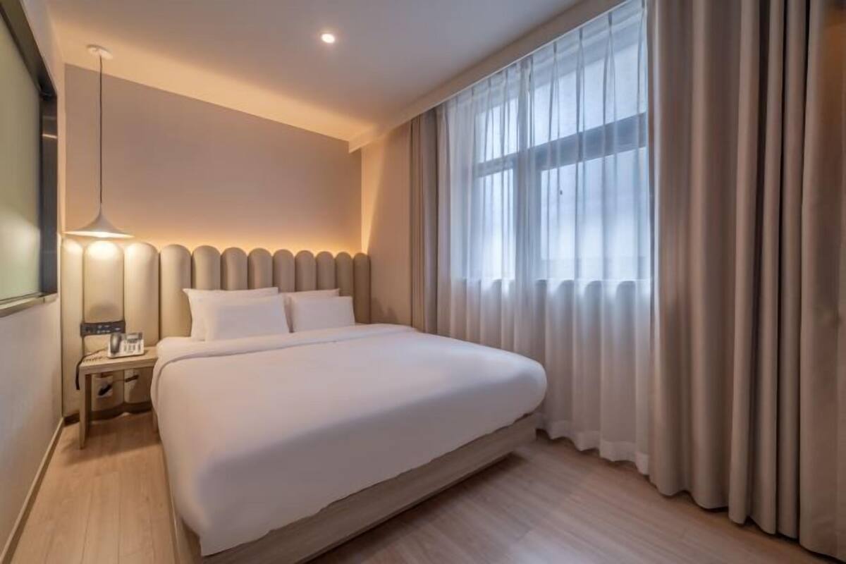 A hotel room with a large bed, a bedside table with a lamp, and a window with curtains.