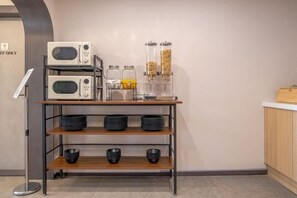 A kitchenette with two microwaves, a coffee maker, and a coffee dispenser on a shelf. - poverta-stay hotel (Gyeongju)
