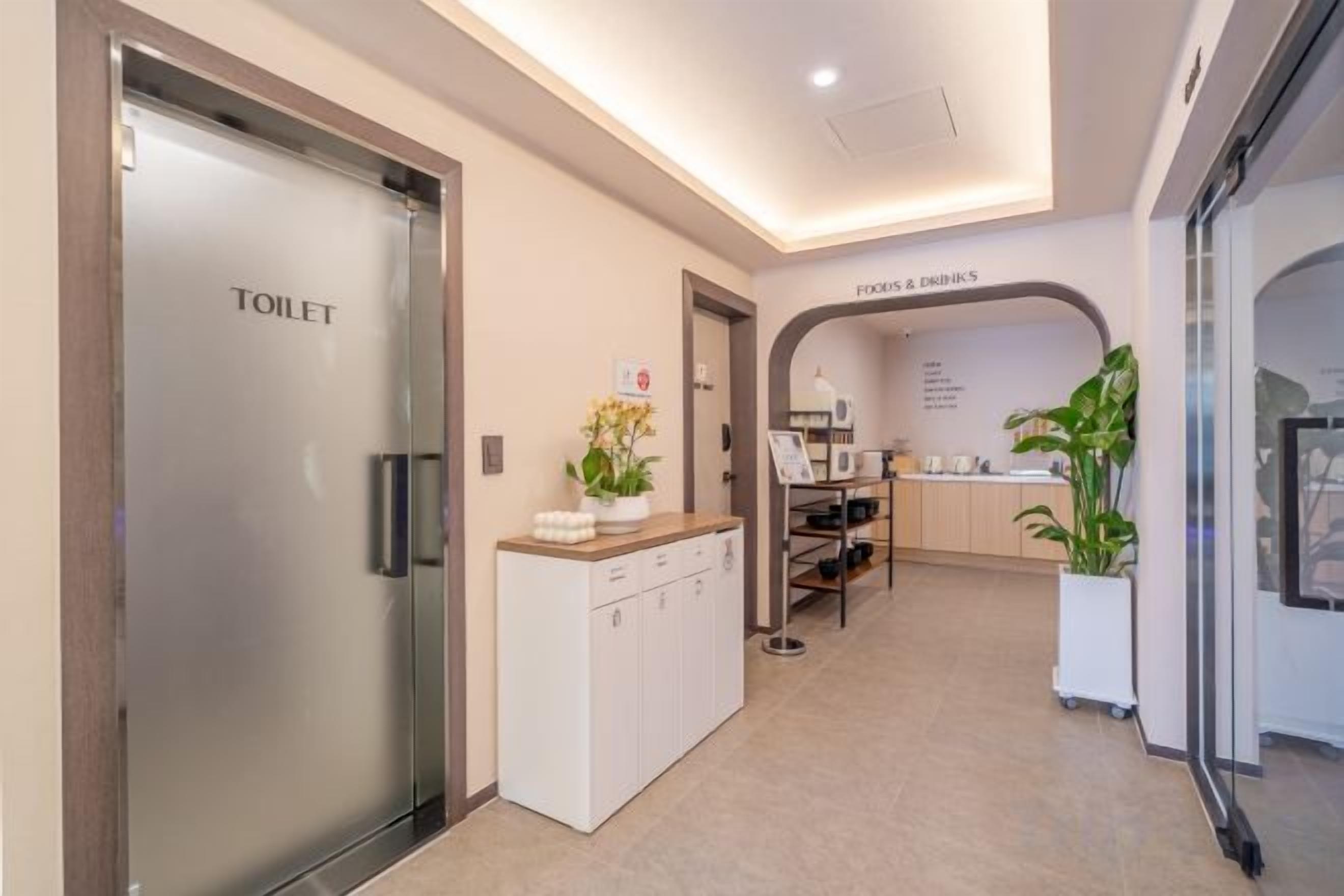 A hotel corridor with a toilet, reception desk, and a kitchenette area.