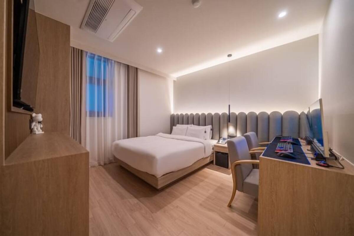 A modern hotel room with a large bed, a desk with a computer, and a TV.