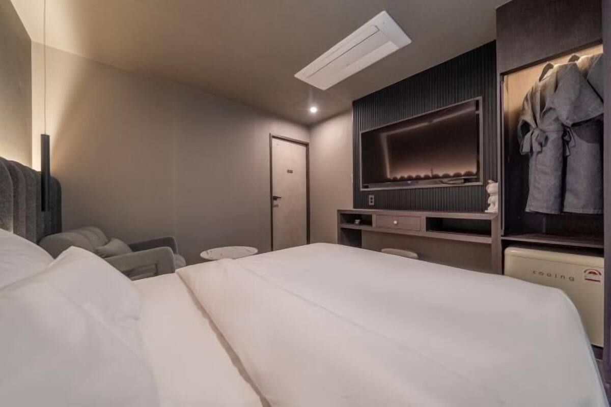 A modern hotel room with a large bed, a seating area with chairs, a built-in TV, and a robe rack.