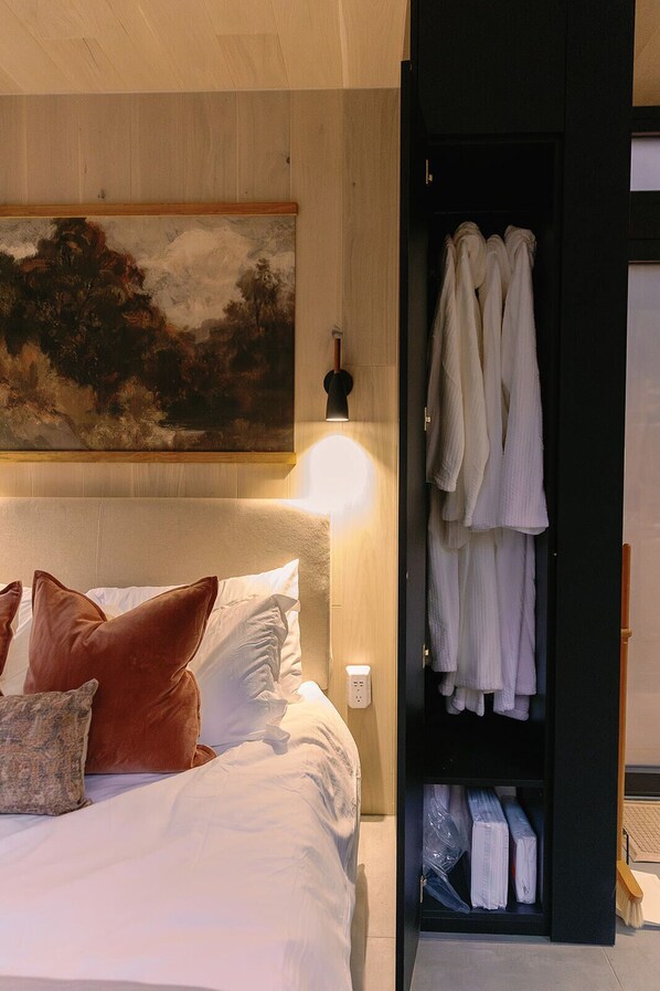 Une chambre à coucher avec un lit, des oreillers, un tableau au mur et une armoire contenant des serviettes.