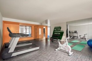 Une salle de sport moderne équipée de tapis de course, de vélos d’appartement et d’appareils d’exercice.