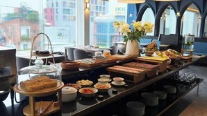 Un bufé de desayuno con diversas opciones de comida y vista a la ciudad a través de amplias ventanas.