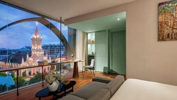 Una habitación de hotel moderna con un ventanal grande, un sofá, una mesita y una silla.