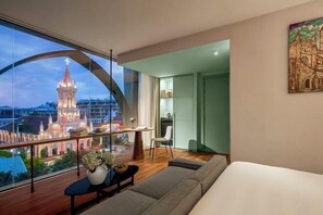 Una habitación de hotel moderna con un ventanal grande, un sofá, una mesita y una silla.