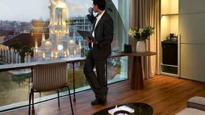 Un hombre con traje de pie junto a una ventana con vistas a un paisaje urbano y una iglesia.