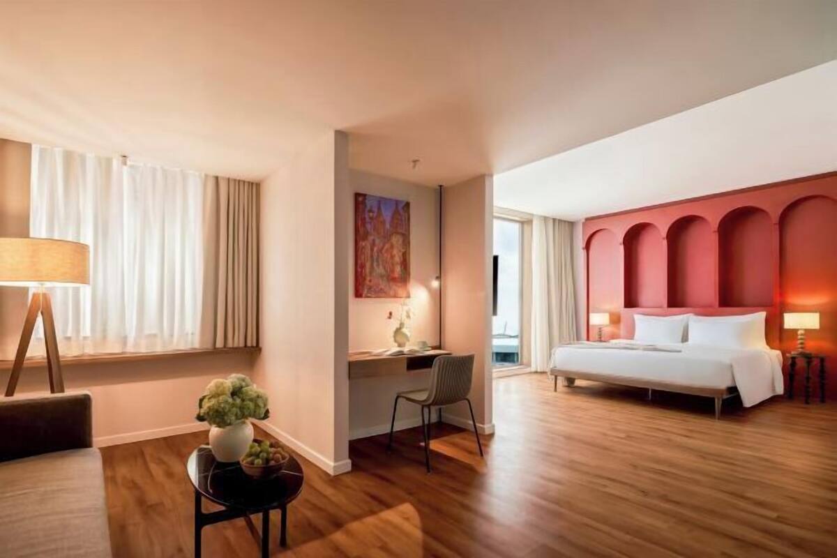 Une chambre d’hôtel avec un lit, un bureau, une chaise et une grande fenêtre avec des rideaux.