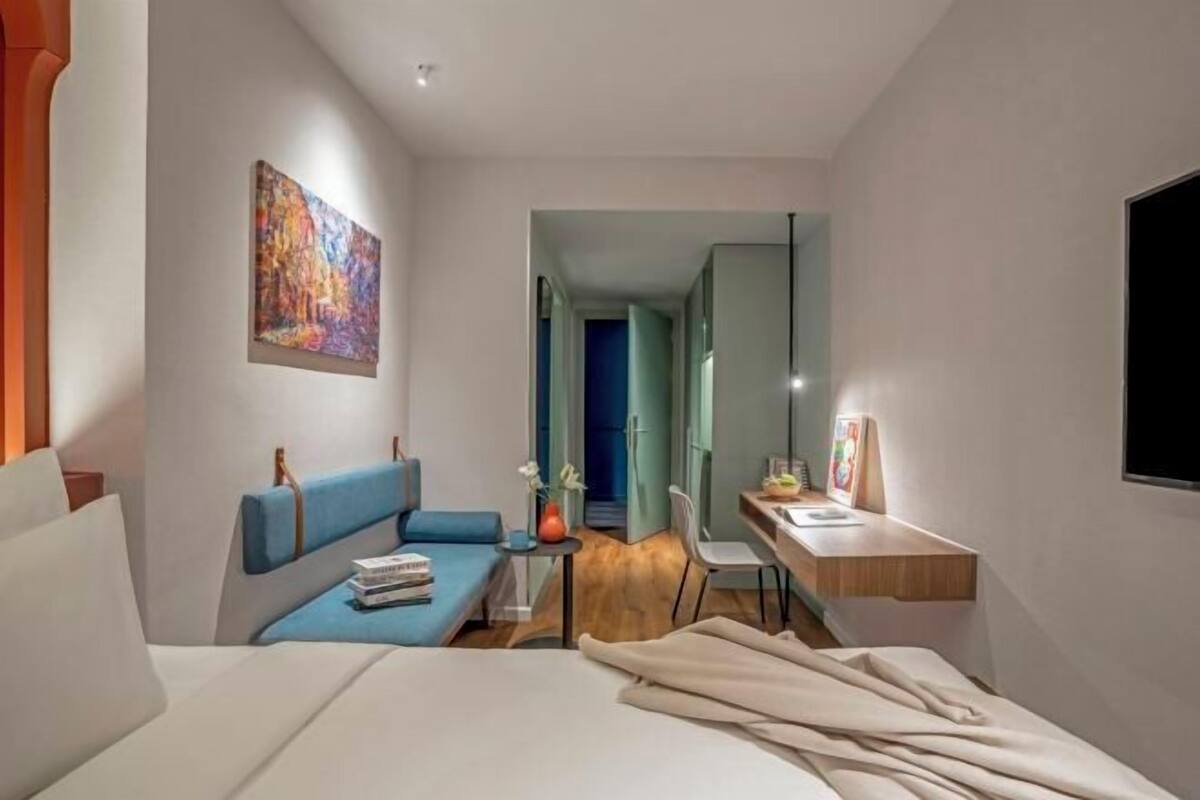 Une chambre d’hôtel moderne avec un lit, un canapé bleu, un bureau et un tableau au mur.