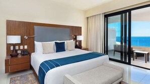 A hotel room with a large bed, a bench, a nightstand with a lamp, and a view of the ocean through a sliding glass door.