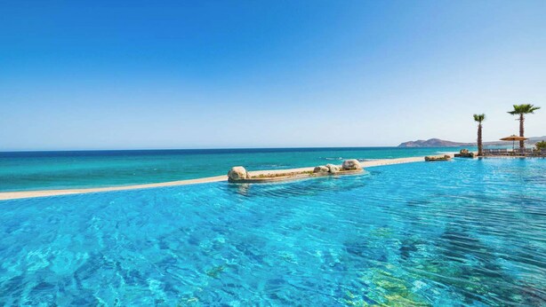 A clear blue pool with a view of the sea and a sandy beach.