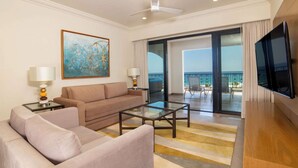 A hotel room with a sofa, a coffee table, a TV, a painting, and a balcony with a view.