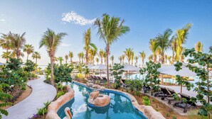 A pool area with palm trees, lounge chairs, and a winding path.