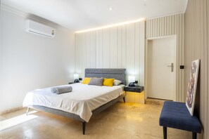 A modern bedroom with a bed, bedside tables, a bench, and a door.
