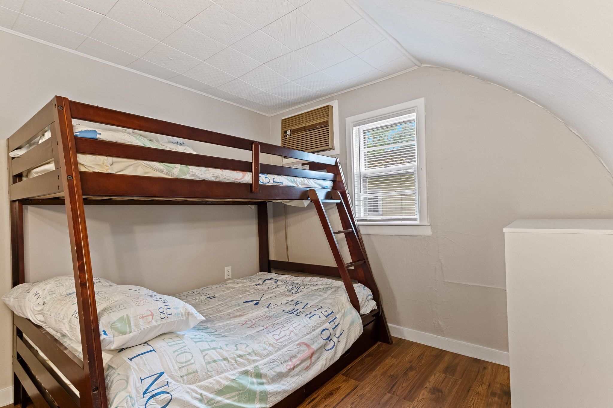 A bunk bed with a ladder, a window with blinds, and a white ceiling.