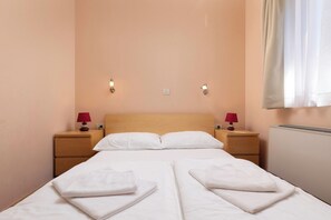 Une chambre d’hôtel avec un lit double, deux tables de chevet avec des lampes, un luminaire fixé au mur et un radiateur.
