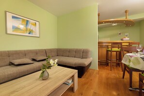 Un salon comprenant un canapé d’angle, une table basse en bois ornée d’un vase de fleurs, et un coin repas avec des chaises et une table en bois.