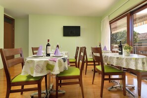 Un coin repas avec des chaises et des tables en bois, un téléviseur à écran plat fixé au mur et une fenêtre avec des rideaux.