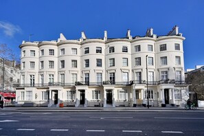 Ein mehrgeschossiges Gebäude mit einer symmetrischen Fassade, großen Fenstern und einem zentralen Eingang mit einem Portikus.