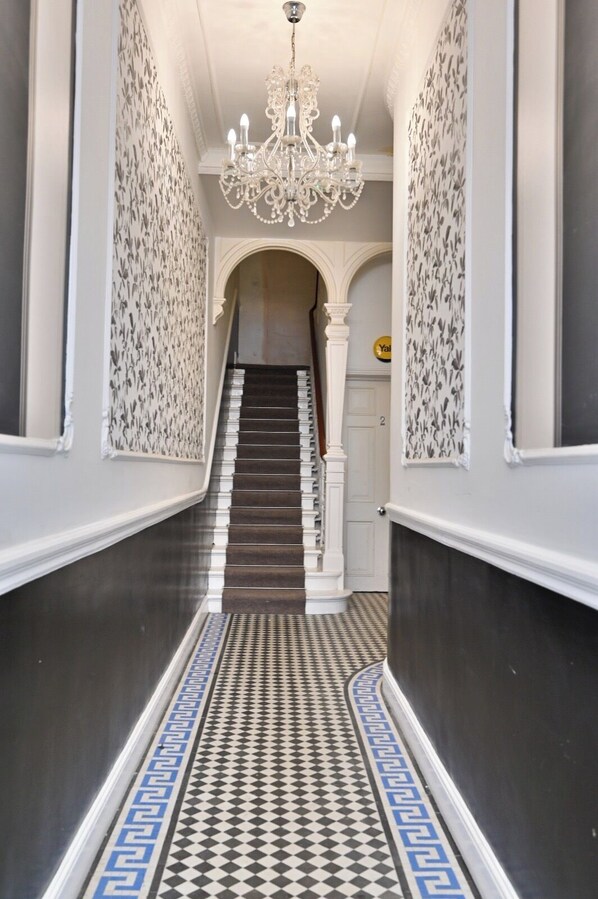Ein Flur mit einem schwarz-weißen Fußboden, einer Chandelüster und einer Treppe zu einer Tür mit der Nummer 2.