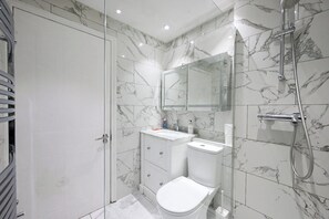 Ein modernes Badezimmer mit einer gläsernen Duschkabine, einer weißen Toilette und einem мрамор-belagten Waschtisch.