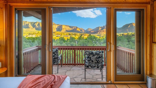A balcony with a view of mountains and a patio area with a bed and chairs. - Casa Del Sol | BBQ, Firepit & Hot Tub with Views (Sedona)