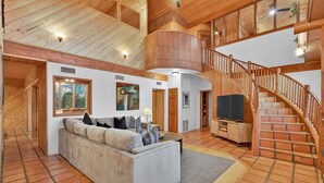A spacious living area with a high ceiling, wooden staircase, and a large sofa. - Casa Del Sol | BBQ, Firepit & Hot Tub with Views (Sedona)