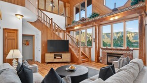 A spacious living room with a large TV, comfortable seating, a fireplace, and a scenic mountain view. - Casa Del Sol | BBQ, Firepit & Hot Tub with Views (Sedona)