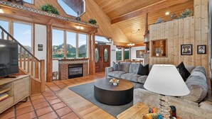 A spacious living room with a fireplace, a large sofa, and a television. - Casa Del Sol | BBQ, Firepit & Hot Tub with Views (Sedona)