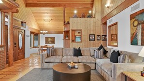 A cozy living room with a sectional sofa, a round coffee table, and a dining area with a wooden table and chairs. - Casa Del Sol | BBQ, Firepit & Hot Tub with Views (Sedona)