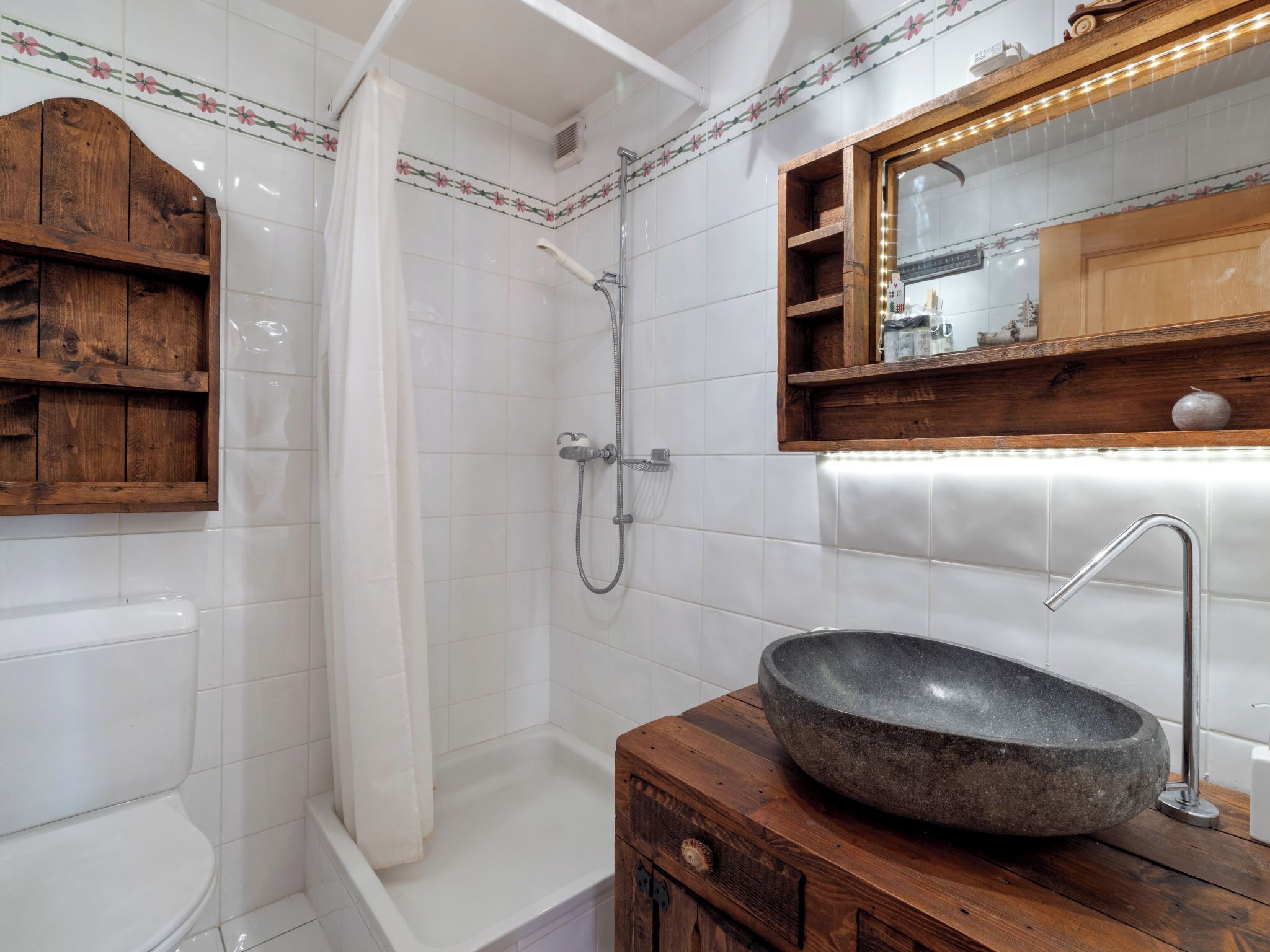 A bathroom with a shower, toilet, and a wooden vanity with a stone sink.