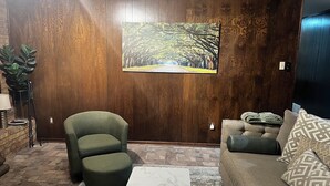 Un salon avec un mur lambrissé en bois, un fauteuil vert, un canapé beige, un tapis à motifs et une table basse en marbre.